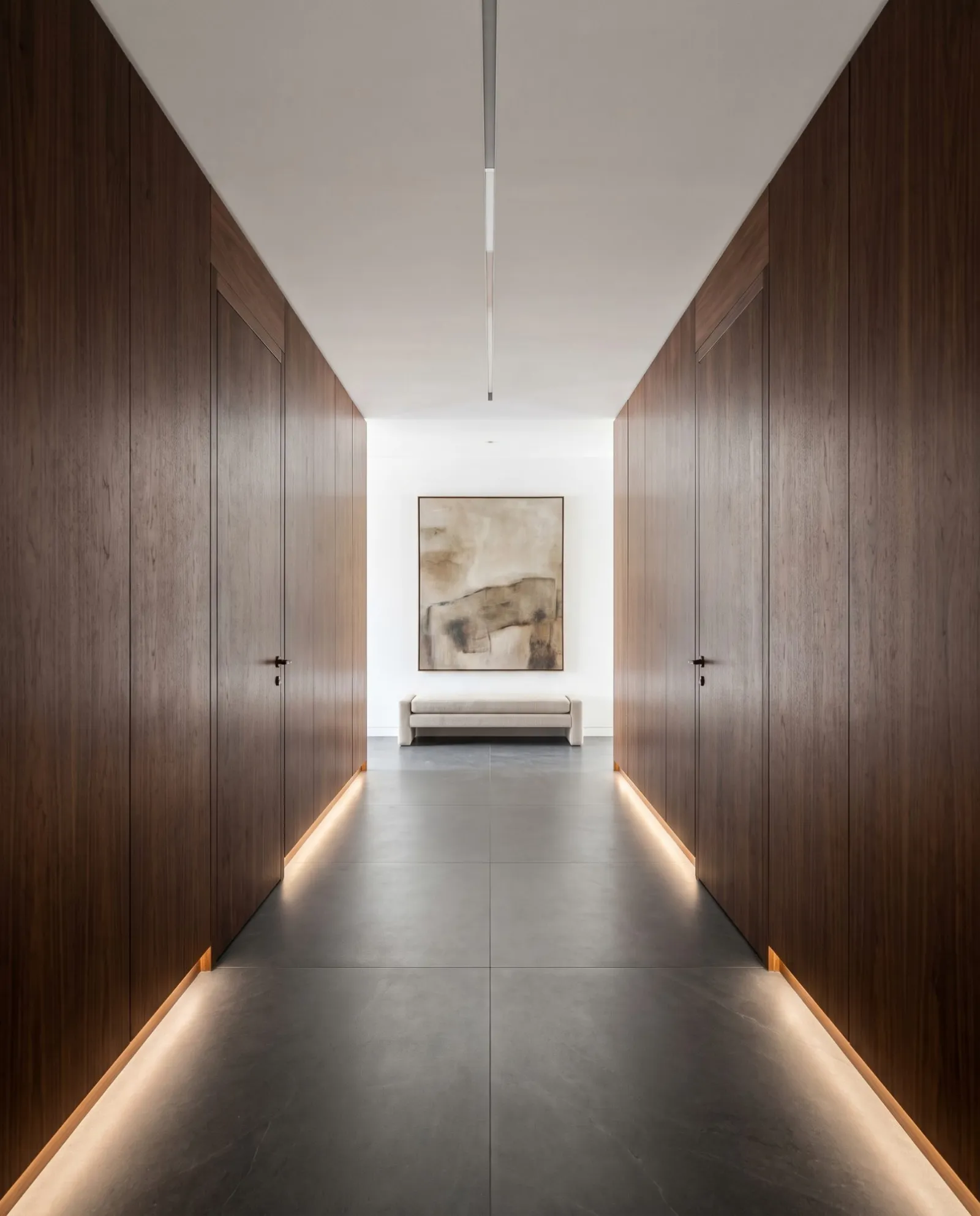 A corridor of walnut panels with flush, concealed doors and light at the floor